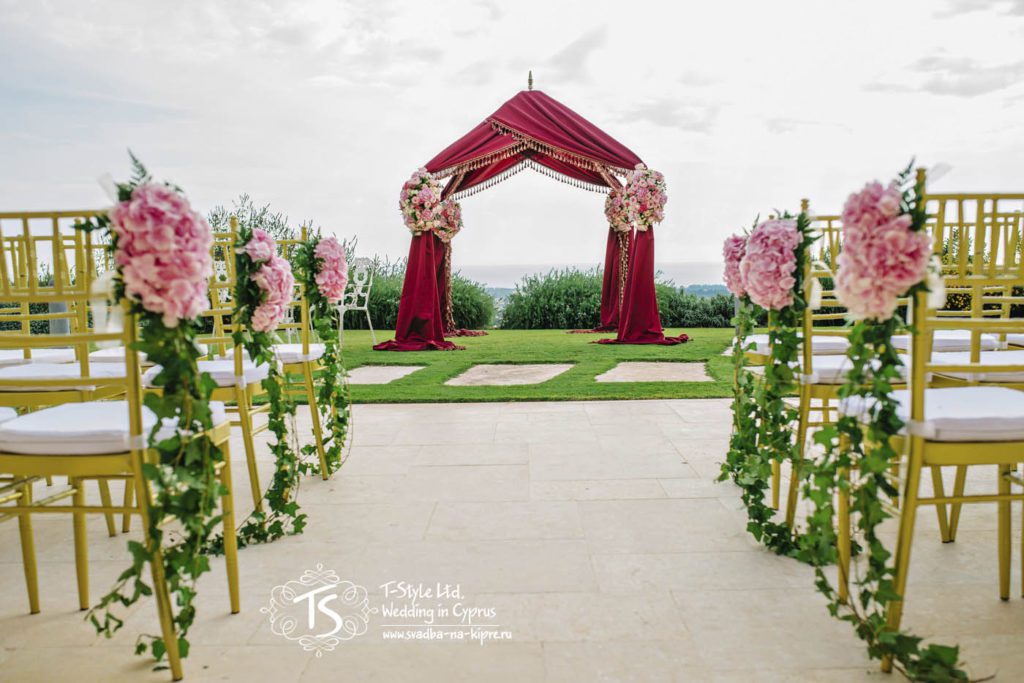 Арка-шатер в цвете марсала, украшенная композициями из розовых роз и золотыми стульями чиавари, украшенными композициями из гортензии и плюща