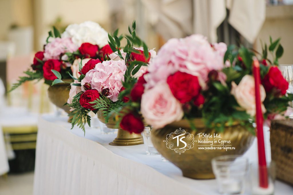 Три низкие вазы золотого цвета с композициями из розовых роз сорта Авалаш, красных пионовидных роз, розовой гортензии с небольшим добавлением зелени